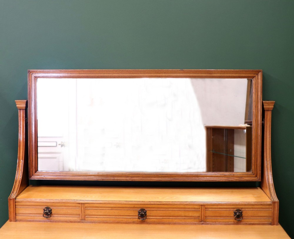 A late Victorian light walnut dressing table featuring an attached rectangular mirror, three small upper drawers, two panelled side cupboards, and turned legs with castors. View VI