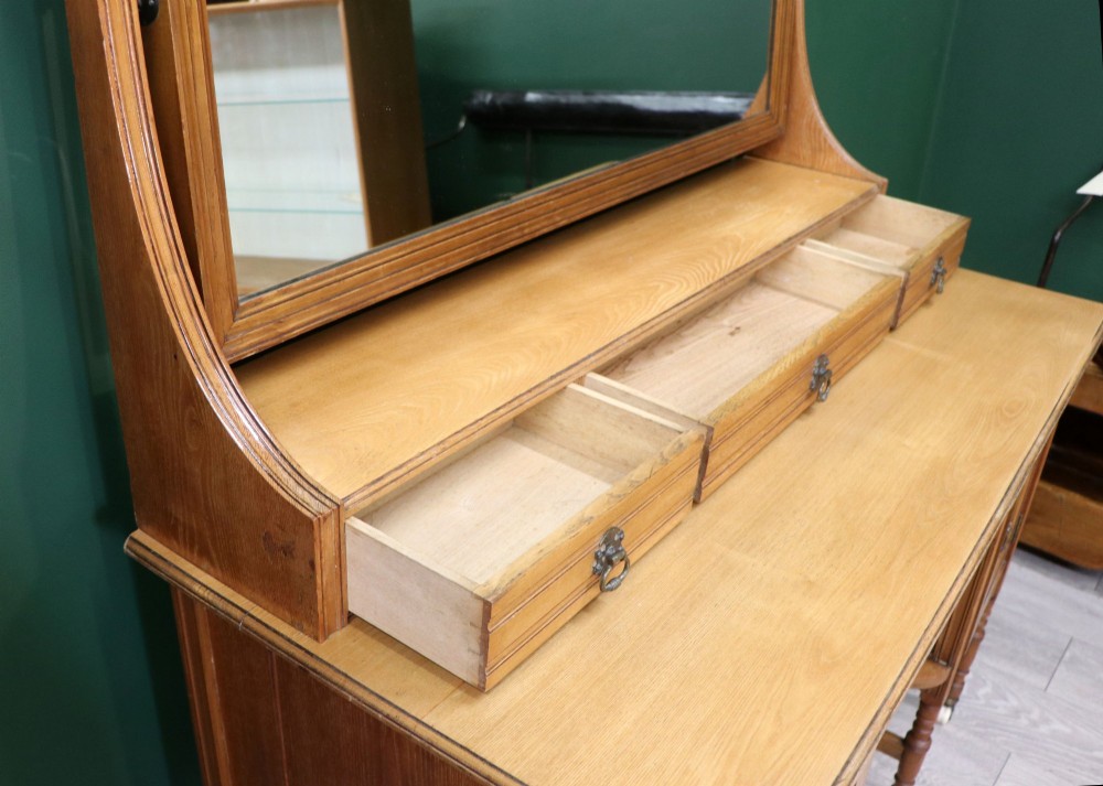 A late Victorian light walnut dressing table featuring an attached rectangular mirror, three small upper drawers, two panelled side cupboards, and turned legs with castors. View IX