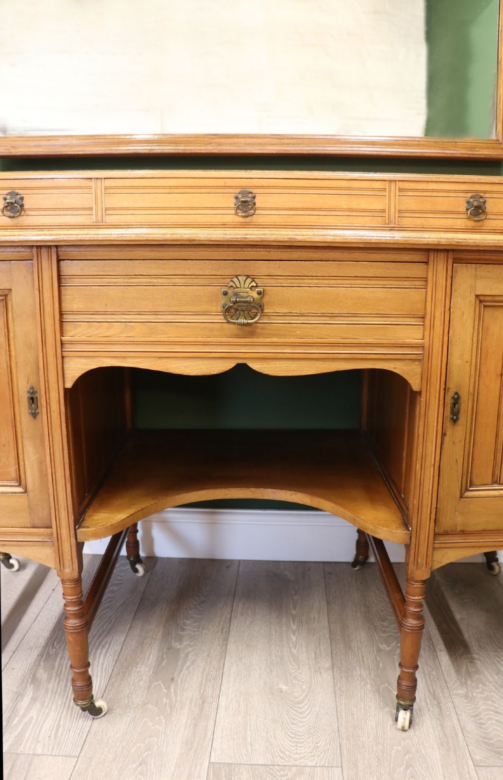 A late Victorian light walnut dressing table featuring an attached rectangular mirror, three small upper drawers, two panelled side cupboards, and turned legs with castors. View XIII