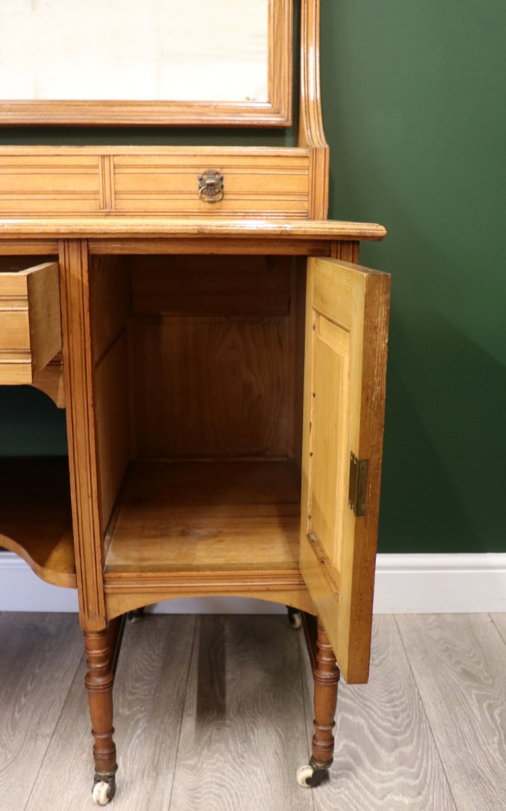 A late Victorian light walnut dressing table featuring an attached rectangular mirror, three small upper drawers, two panelled side cupboards, and turned legs with castors. View XIV