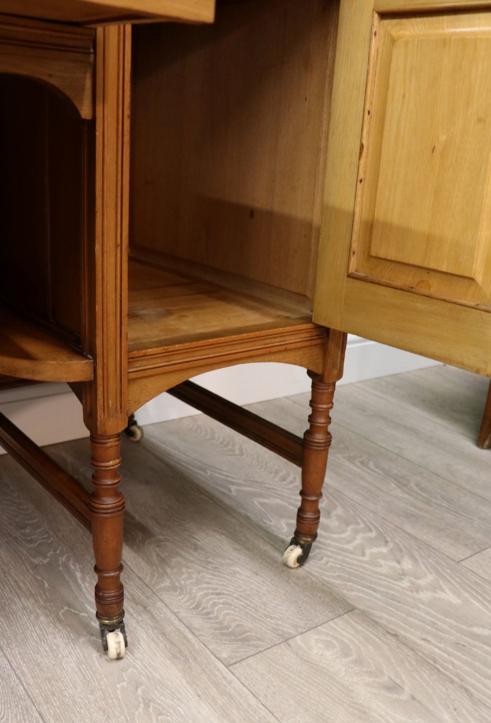 A late Victorian light walnut dressing table featuring an attached rectangular mirror, three small upper drawers, two panelled side cupboards, and turned legs with castors. View XV