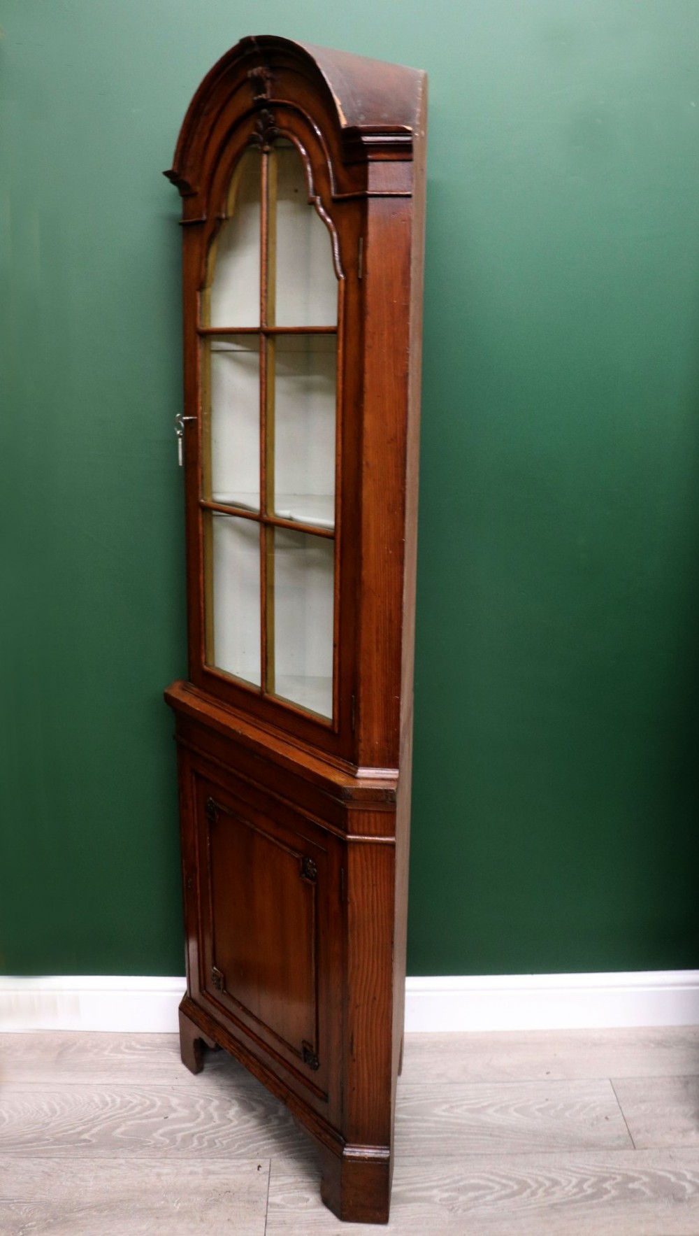 An early 20th-century floor-standing oak corner cabinet featuring an arched glazed upper door and a solid wood lower cupboard door. View IV