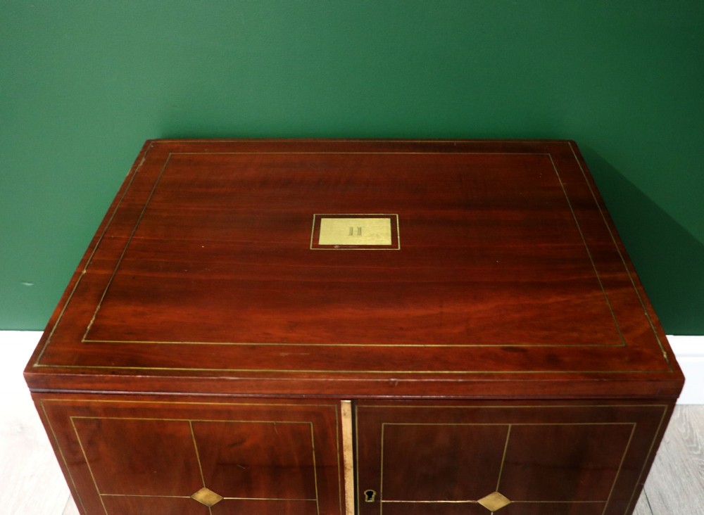 A mahogany campaign style collectors cabinet featuring geometric brass line inlays, twin front doors, a brass central keyhole, and shaped feet. View VII