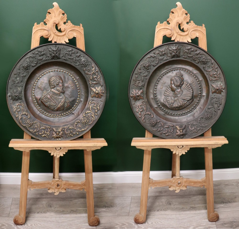 Pair of circular relief-embossed copper wall chargers depicting profile portraits of King Henry IV and Queen Marie de Medicis surrounded by floral and mask borders.