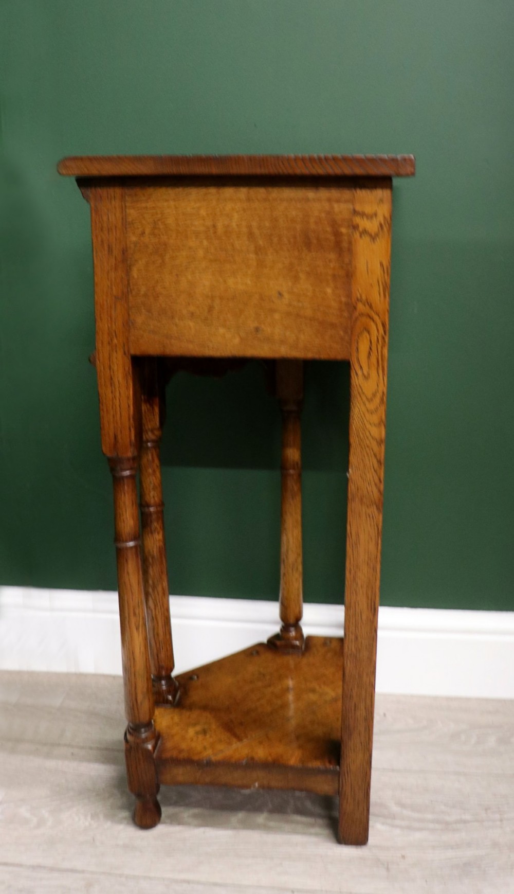 An antique golden oak corner table featuring turned legs, a single drawer with a brass drop handle, a shaped frieze, and a low tier shelf. View V