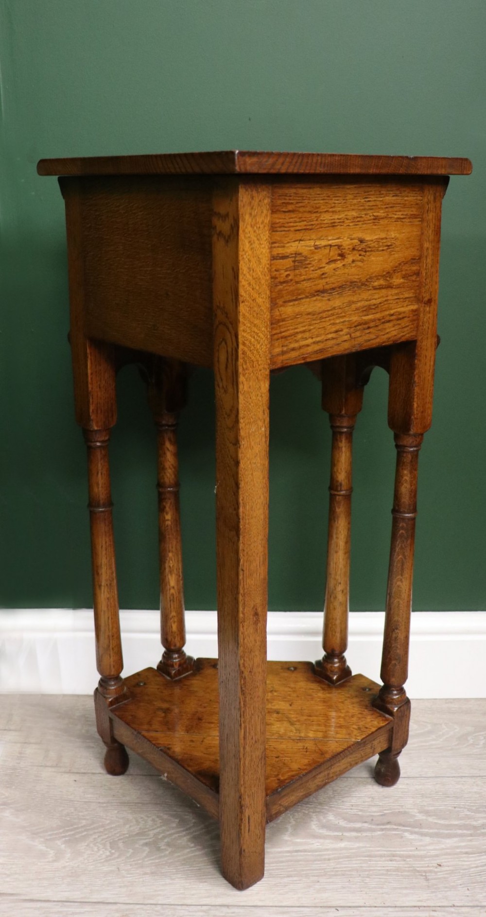 An antique golden oak corner table featuring turned legs, a single drawer with a brass drop handle, a shaped frieze, and a low tier shelf. View VI