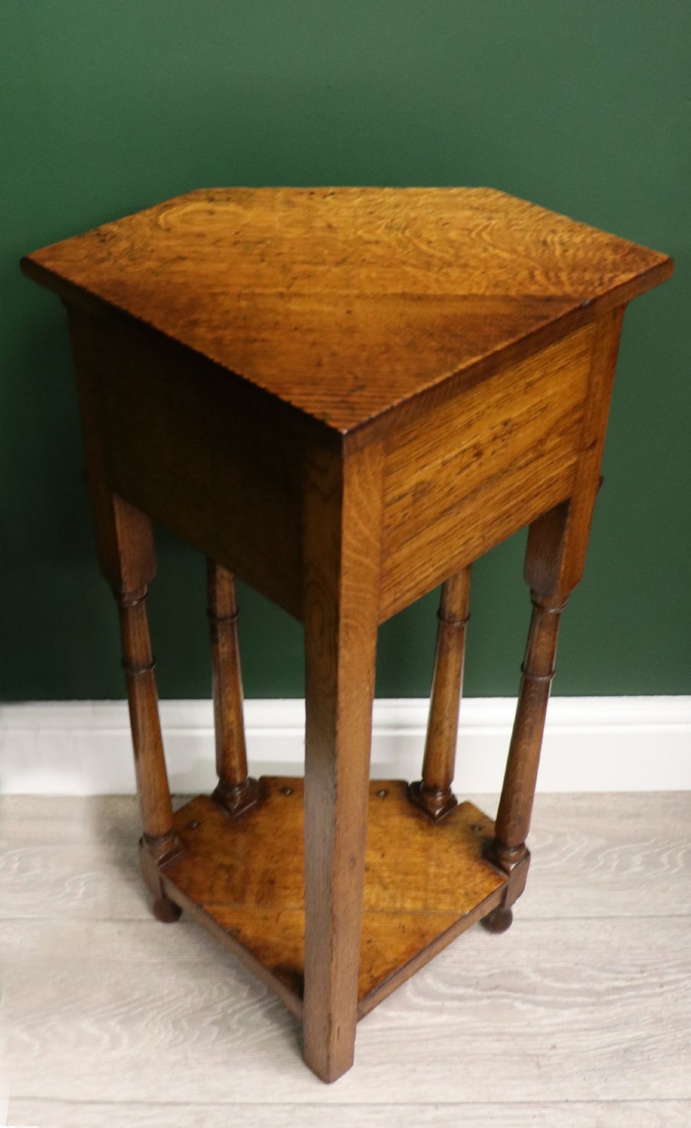 An antique golden oak corner table featuring turned legs, a single drawer with a brass drop handle, a shaped frieze, and a low tier shelf. View VII