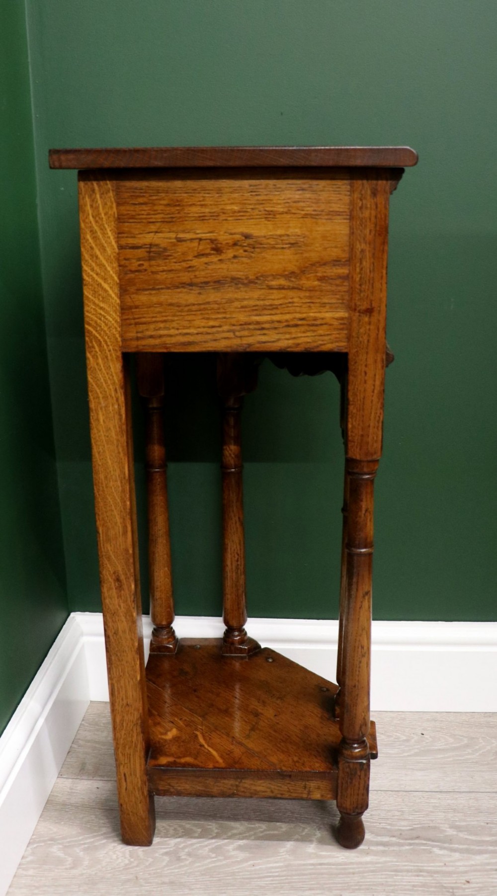 An antique golden oak corner table featuring turned legs, a single drawer with a brass drop handle, a shaped frieze, and a low tier shelf. View VIII