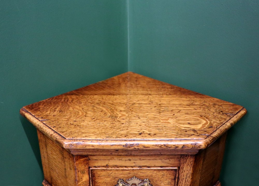 An antique golden oak corner table featuring turned legs, a single drawer with a brass drop handle, a shaped frieze, and a low tier shelf. View X