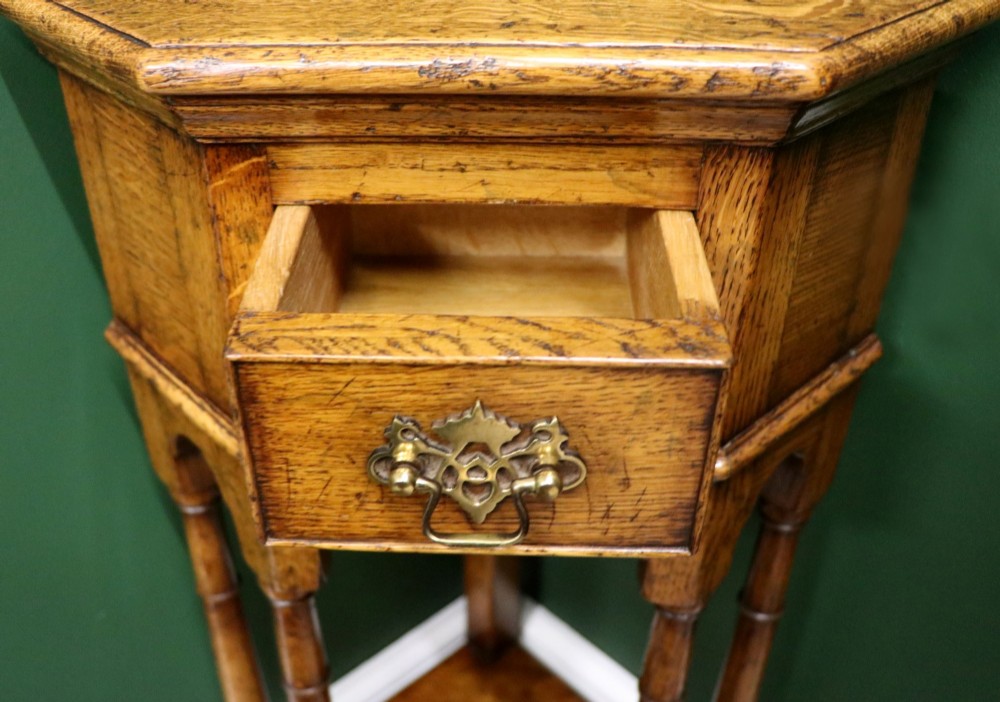 An antique golden oak corner table featuring turned legs, a single drawer with a brass drop handle, a shaped frieze, and a low tier shelf. View XI
