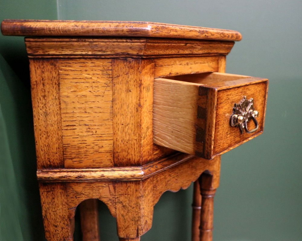 An antique golden oak corner table featuring turned legs, a single drawer with a brass drop handle, a shaped frieze, and a low tier shelf. View XIII