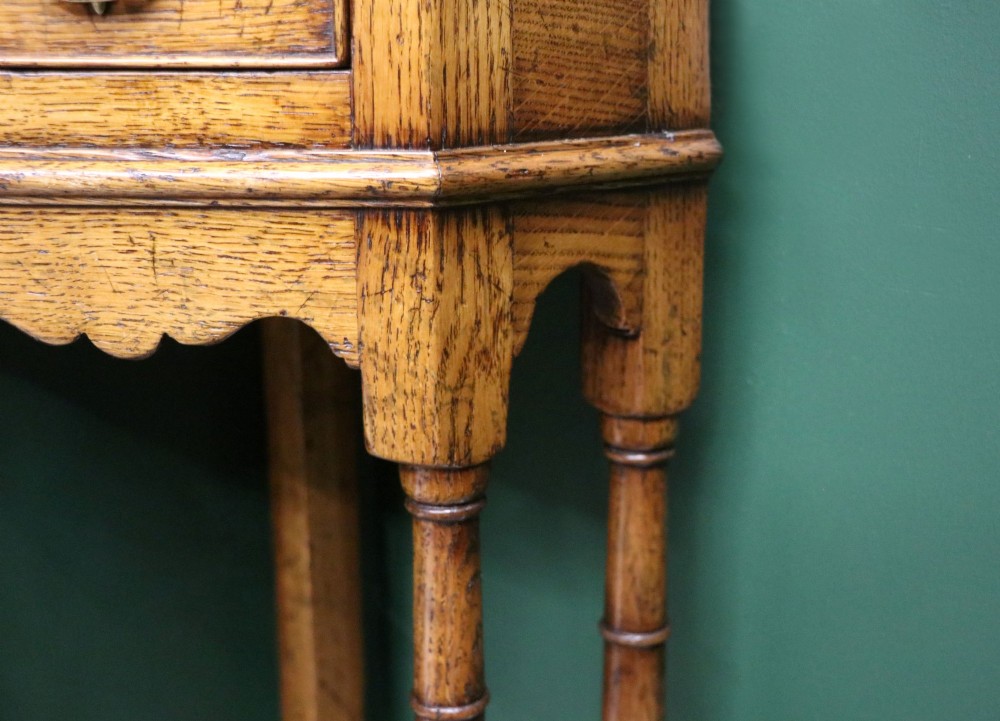 An antique golden oak corner table featuring turned legs, a single drawer with a brass drop handle, a shaped frieze, and a low tier shelf. View XIV