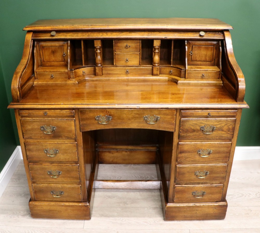 A solid oak roll top desk featuring a retracted slatted tambour top revealing a fitted interior with small drawers and pigeonholes over twin pedestals.