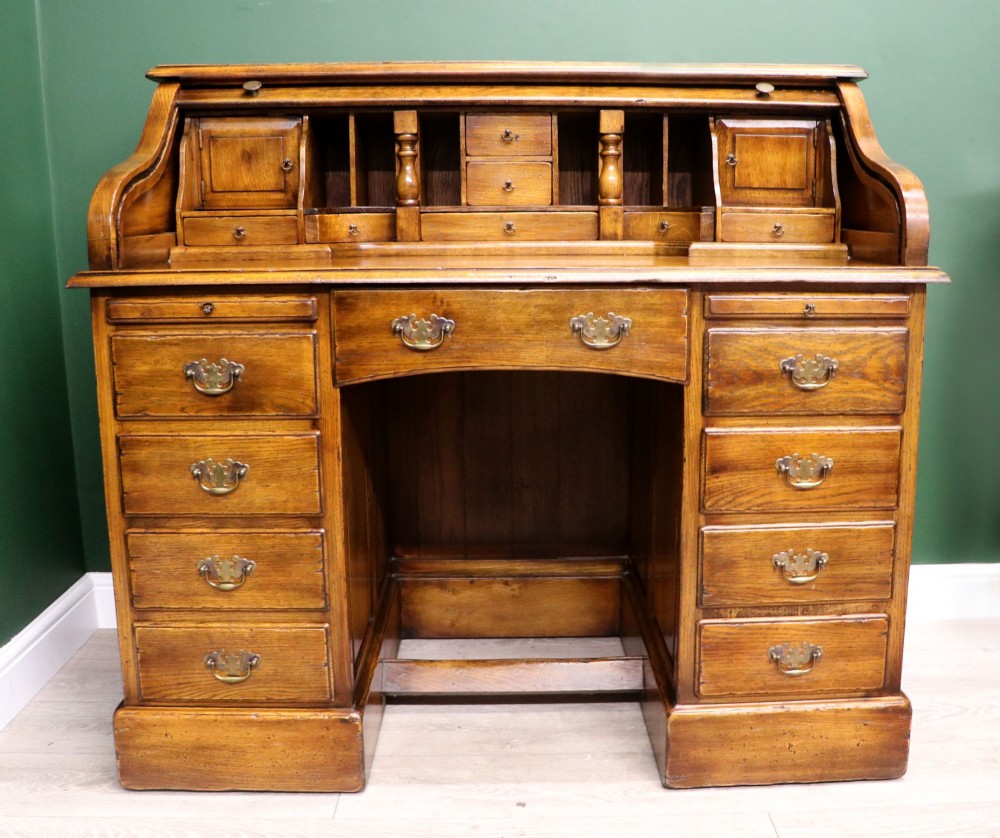 A solid oak roll top desk featuring a retracted slatted tambour top revealing a fitted interior with small drawers and pigeonholes over twin pedestals. View II