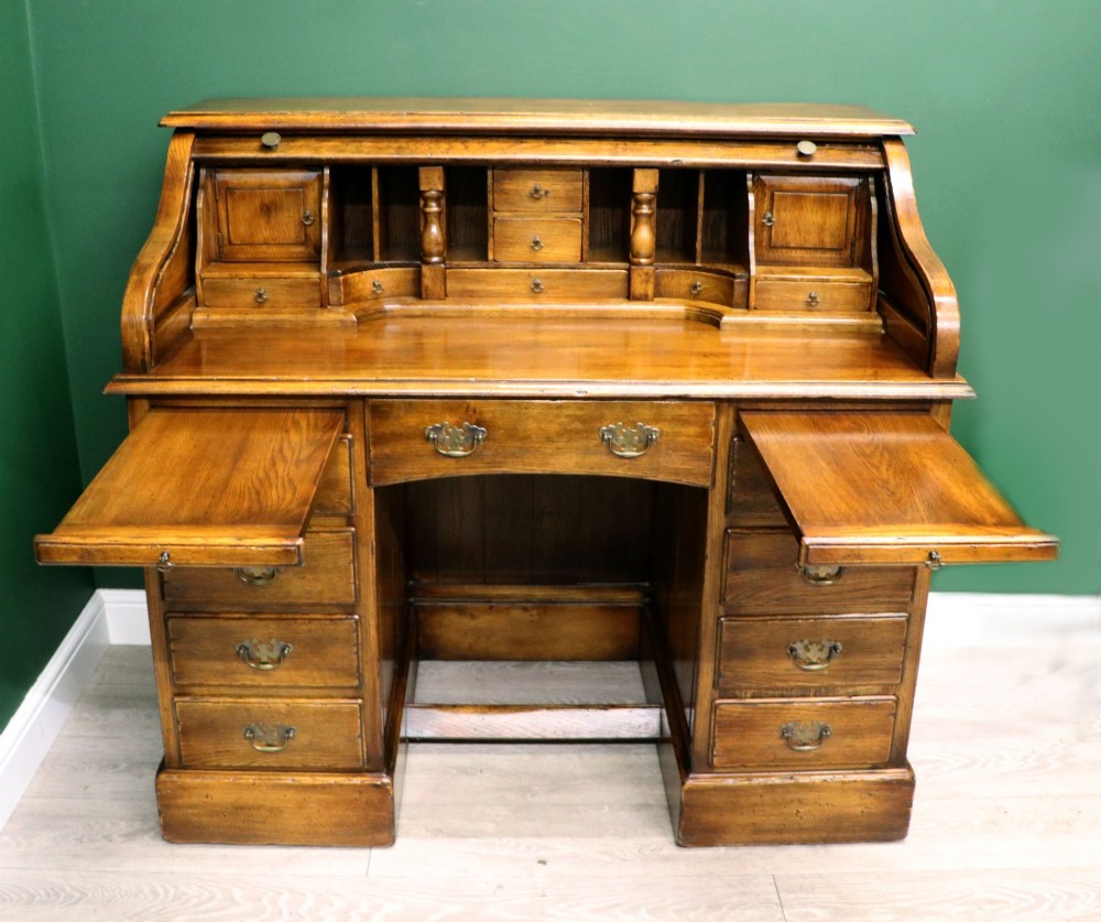 A solid oak roll top desk featuring a retracted slatted tambour top revealing a fitted interior with small drawers and pigeonholes over twin pedestals. View III