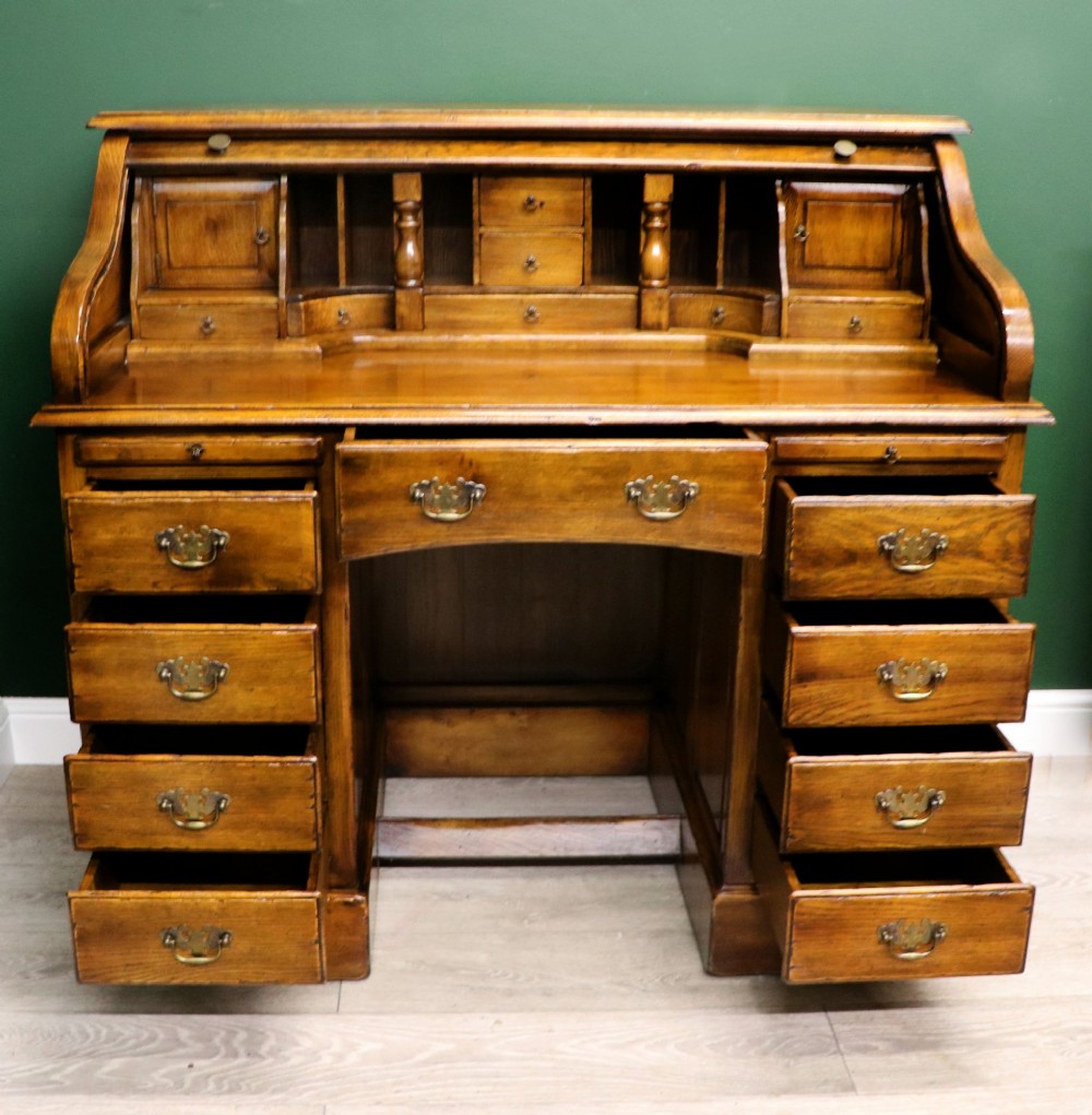A solid oak roll top desk featuring a retracted slatted tambour top revealing a fitted interior with small drawers and pigeonholes over twin pedestals. View IV