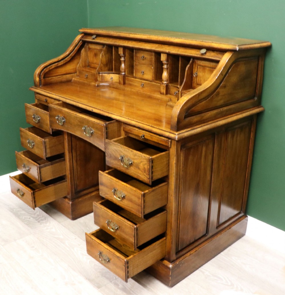 A solid oak roll top desk featuring a retracted slatted tambour top revealing a fitted interior with small drawers and pigeonholes over twin pedestals. View V