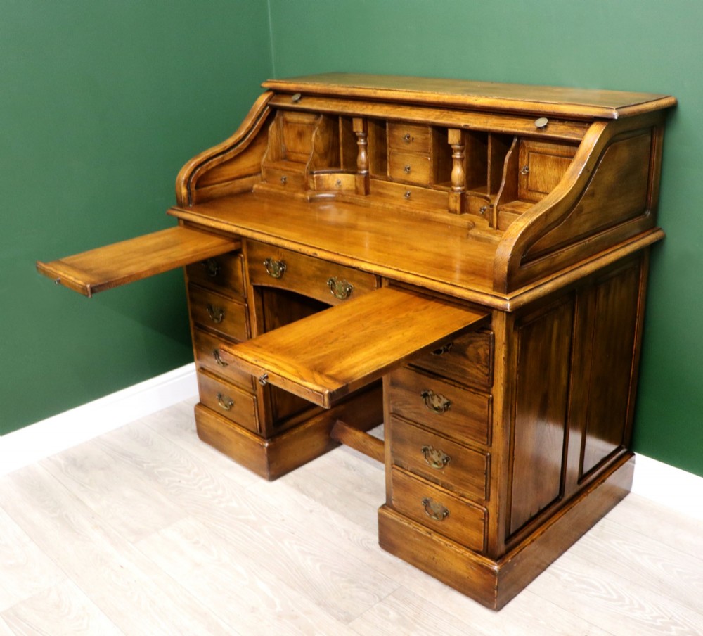 A solid oak roll top desk featuring a retracted slatted tambour top revealing a fitted interior with small drawers and pigeonholes over twin pedestals. View VI