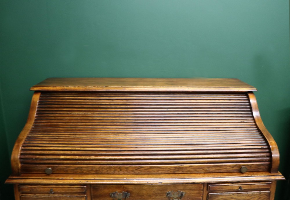 A solid oak roll top desk featuring a retracted slatted tambour top revealing a fitted interior with small drawers and pigeonholes over twin pedestals. View VII