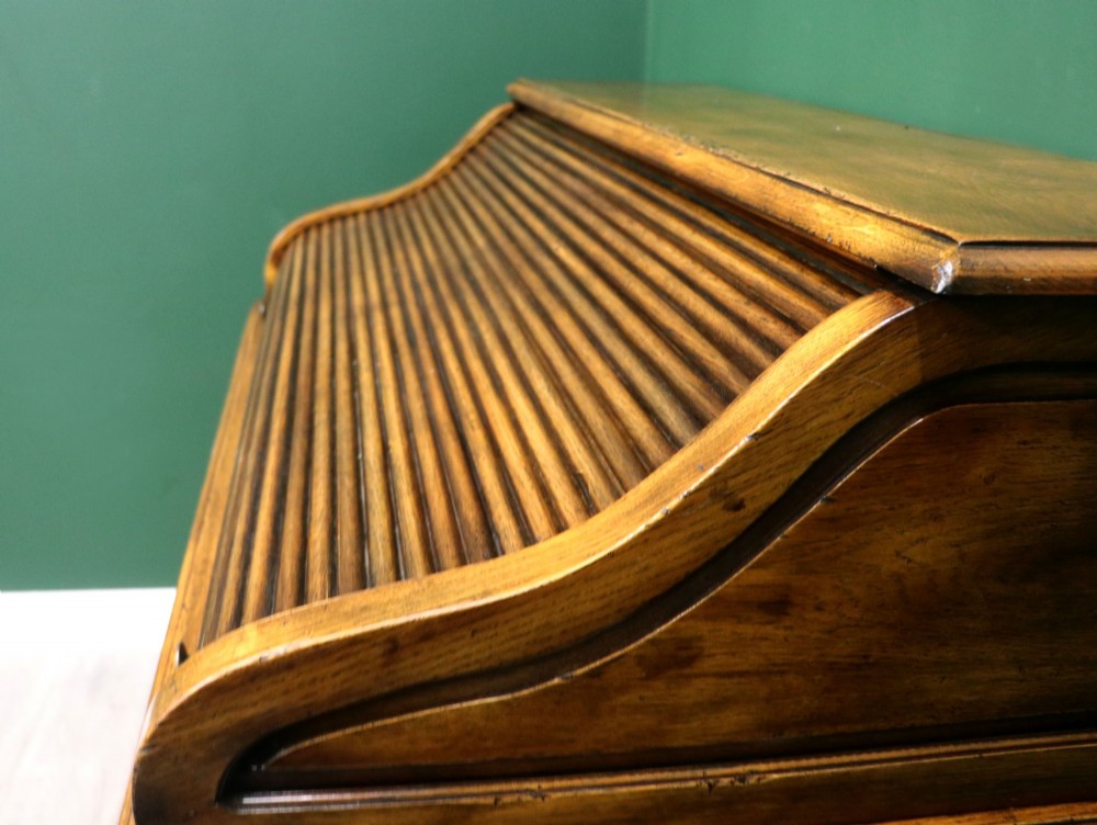 A solid oak roll top desk featuring a retracted slatted tambour top revealing a fitted interior with small drawers and pigeonholes over twin pedestals. View VIII