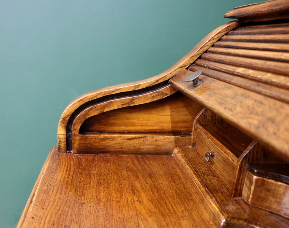 A solid oak roll top desk featuring a retracted slatted tambour top revealing a fitted interior with small drawers and pigeonholes over twin pedestals. View X