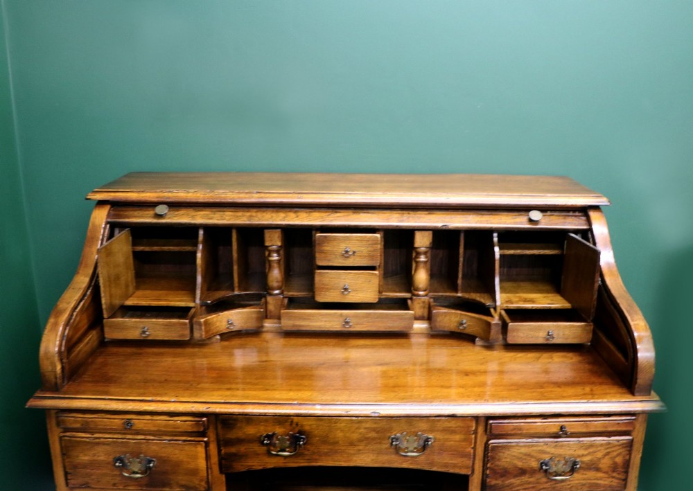 A solid oak roll top desk featuring a retracted slatted tambour top revealing a fitted interior with small drawers and pigeonholes over twin pedestals. View XI