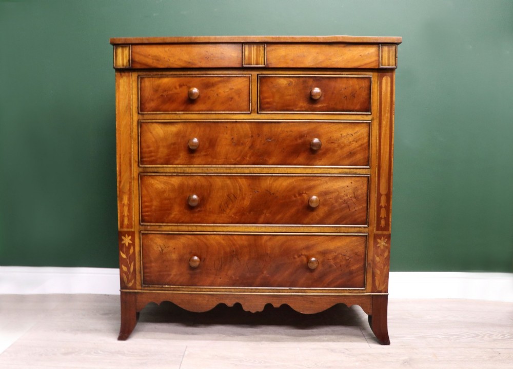 A small Victorian mahogany chest of drawers featuring decorative inlay along the frame, turned wooden knobs, and a shaped apron on curved feet.