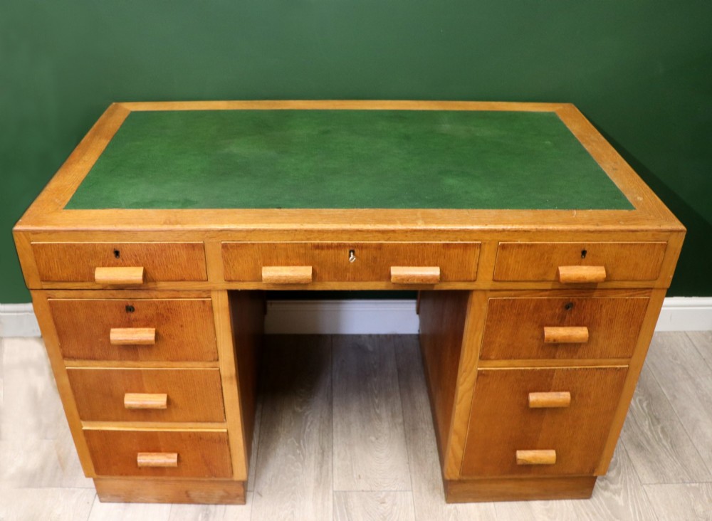 An Art Deco light oak twin pedestal desk featuring a green writing top inset and carved wooden bar drawer handles.