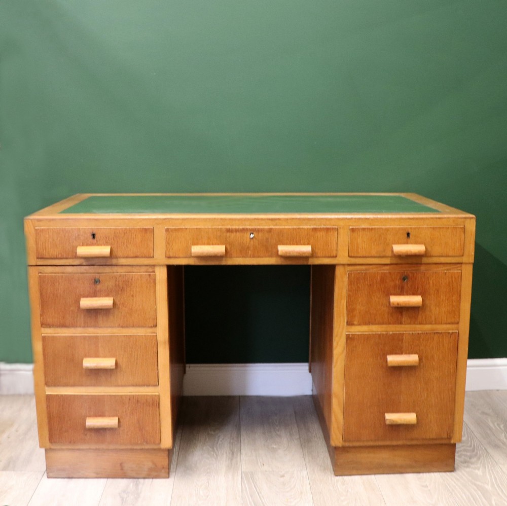 An Art Deco light oak twin pedestal desk featuring a green writing top inset and carved wooden bar drawer handles. View II