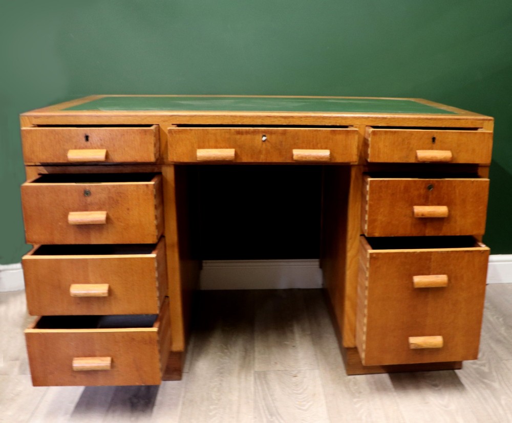 An Art Deco light oak twin pedestal desk featuring a green writing top inset and carved wooden bar drawer handles. View IV