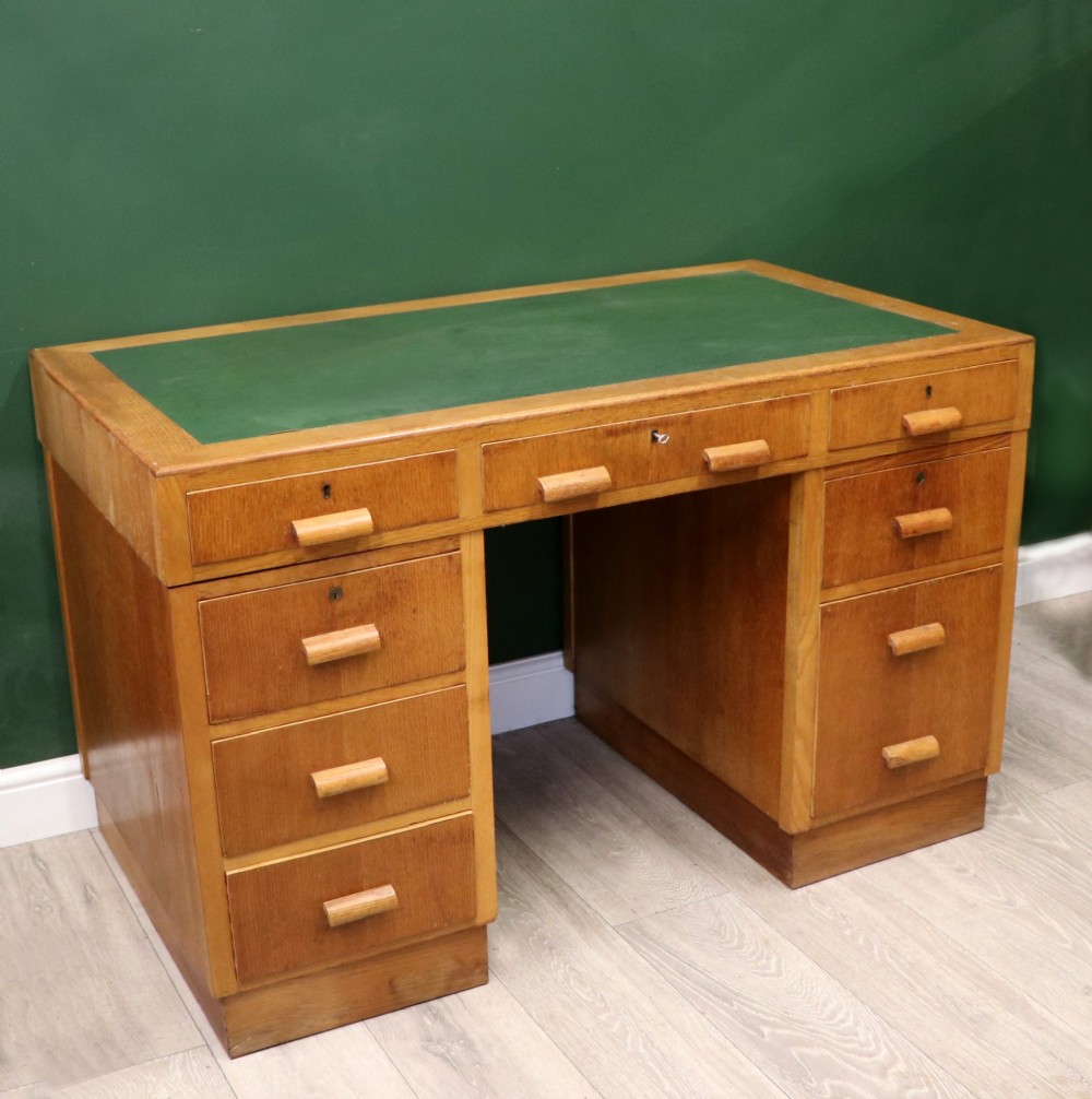 An Art Deco light oak twin pedestal desk featuring a green writing top inset and carved wooden bar drawer handles. View V