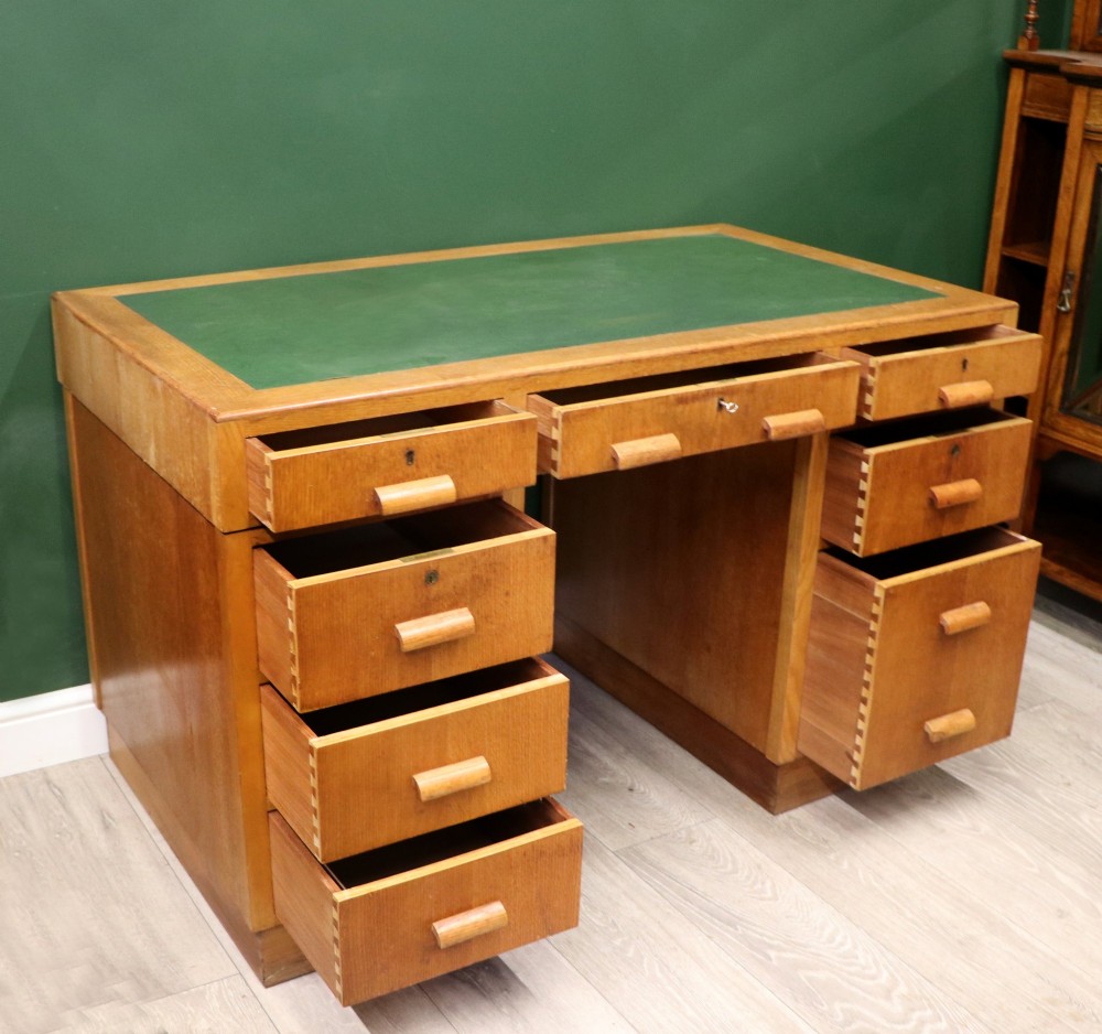 An Art Deco light oak twin pedestal desk featuring a green writing top inset and carved wooden bar drawer handles. View VI