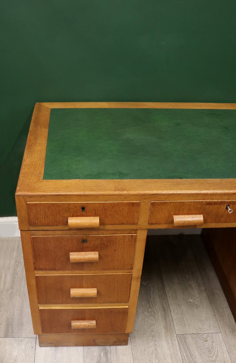 An Art Deco light oak twin pedestal desk featuring a green writing top inset and carved wooden bar drawer handles. View VII