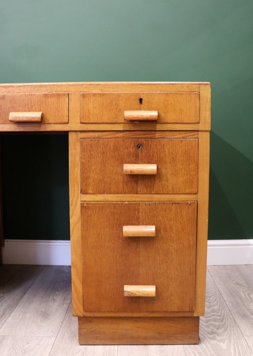 An Art Deco light oak twin pedestal desk featuring a green writing top inset and carved wooden bar drawer handles. View X