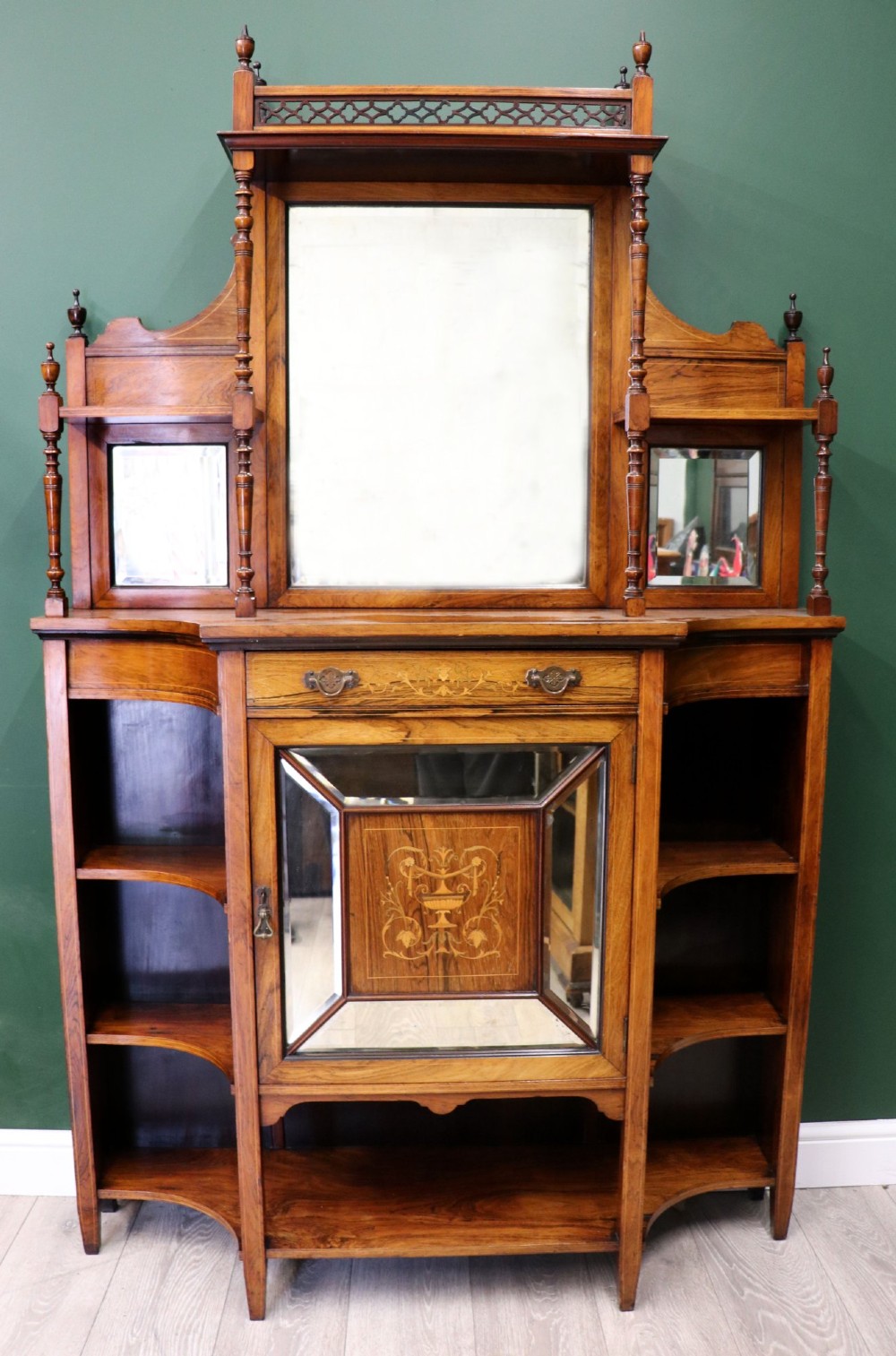 A late Victorian wooden credenza featuring a central inlaid cupboard door, open side shelves, turned spindle pillars, and a multi-pane mirrored back with a fretwork gallery top.