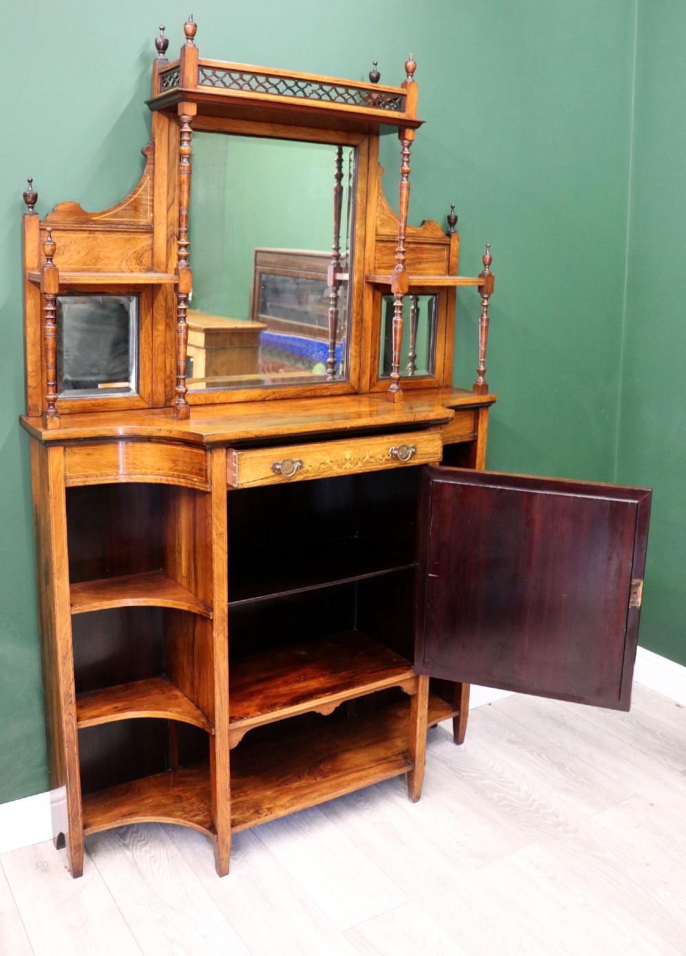 A late Victorian wooden credenza featuring a central inlaid cupboard door, open side shelves, turned spindle pillars, and a multi-pane mirrored back with a fretwork gallery top. View II