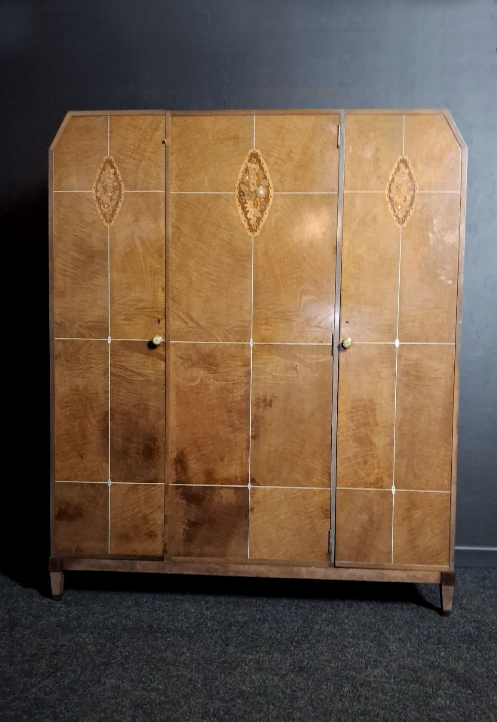 An Art Deco three-door walnut wardrobe featuring geometric panel veneers and oval floral marquetry inlays.