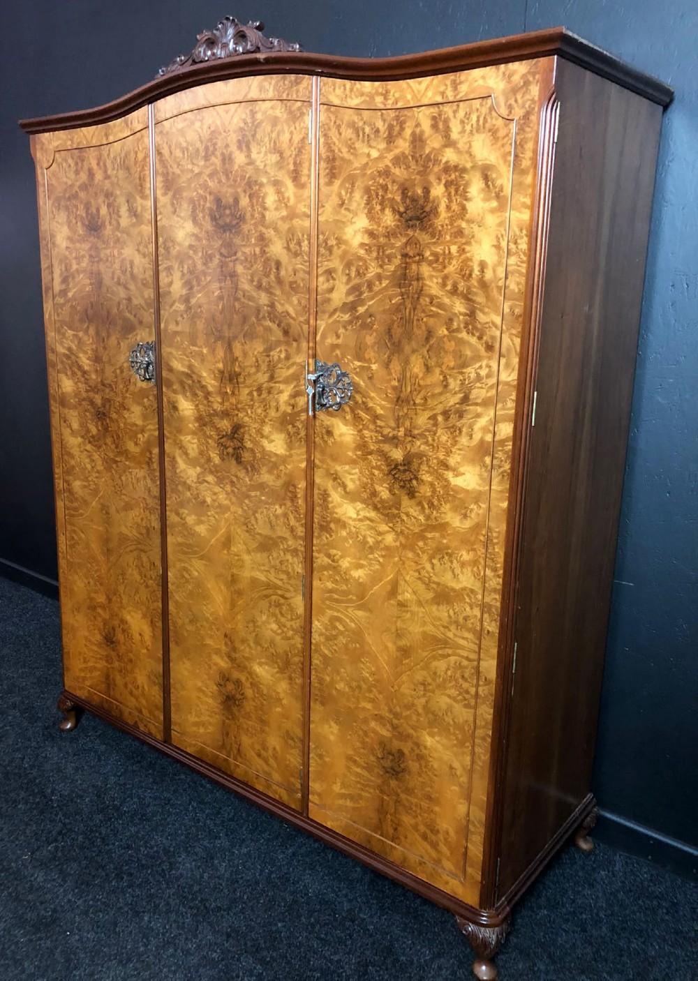 A large Queen Anne revival three-door wardrobe crafted with highly figured burr walnut veneer, featuring carved cresting and decorative metal escutcheons. View II