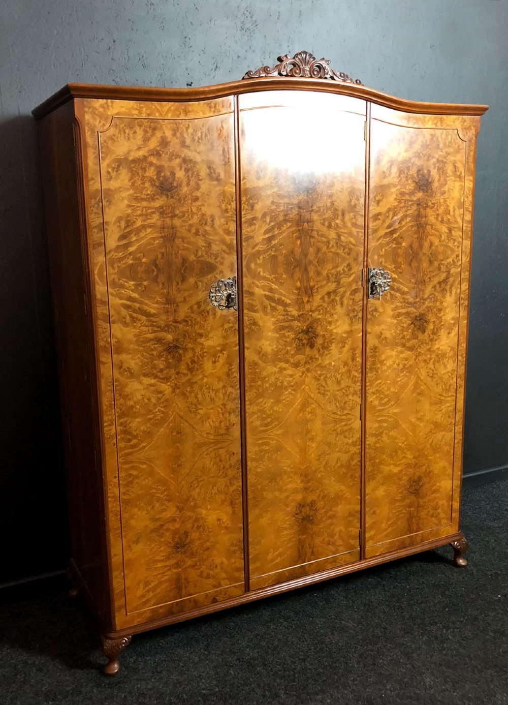 A large Queen Anne revival three-door wardrobe crafted with highly figured burr walnut veneer, featuring carved cresting and decorative metal escutcheons. View III