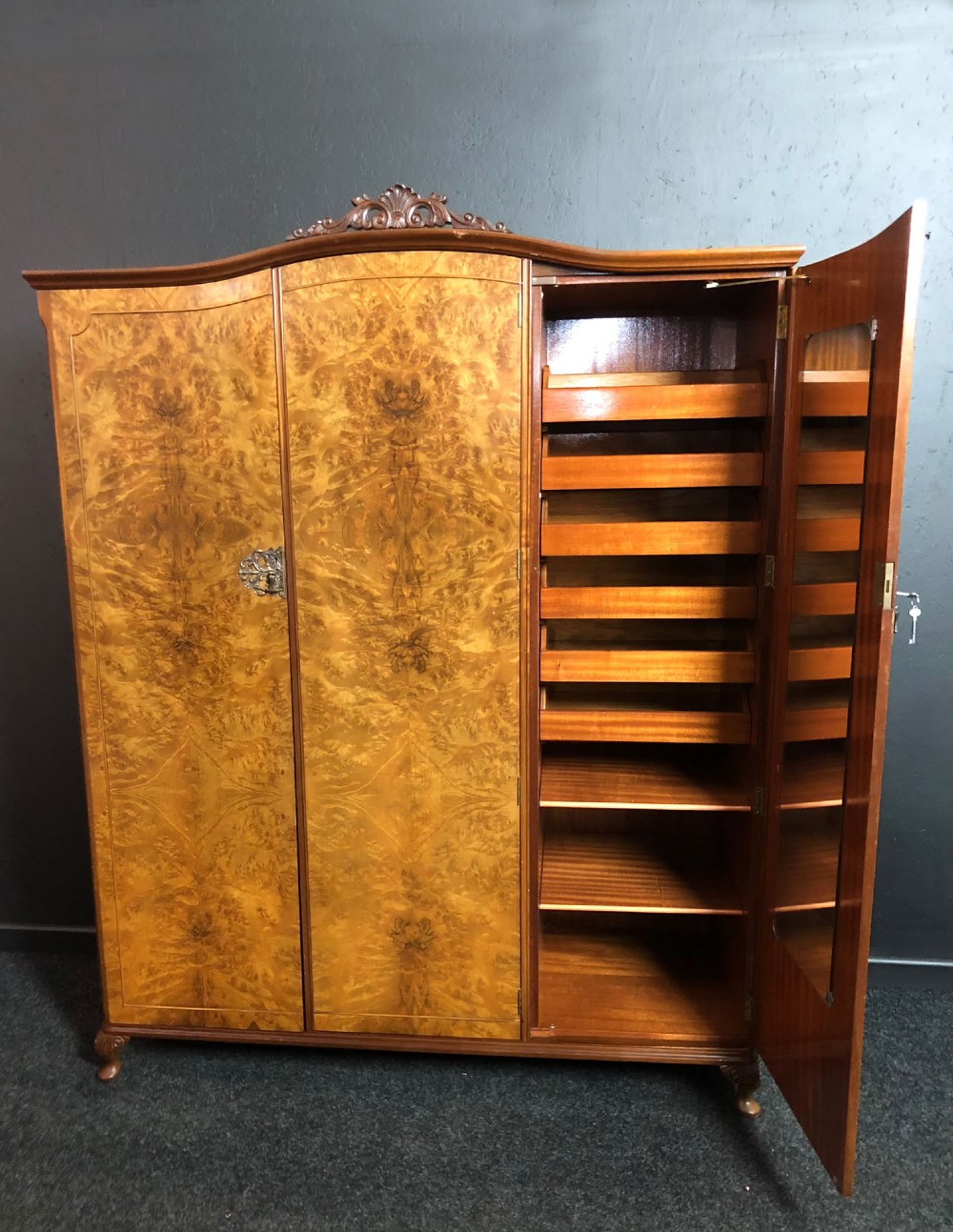 A large Queen Anne revival three-door wardrobe crafted with highly figured burr walnut veneer, featuring carved cresting and decorative metal escutcheons. View IV