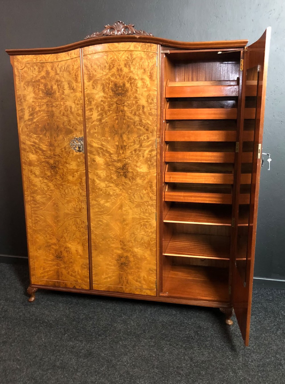 A large Queen Anne revival three-door wardrobe crafted with highly figured burr walnut veneer, featuring carved cresting and decorative metal escutcheons. View V