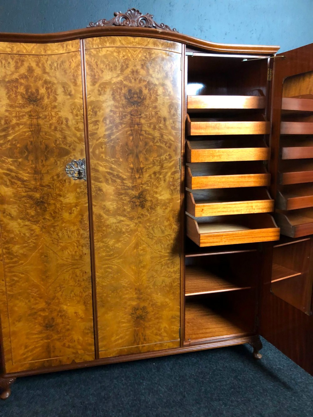 A large Queen Anne revival three-door wardrobe crafted with highly figured burr walnut veneer, featuring carved cresting and decorative metal escutcheons. View VI