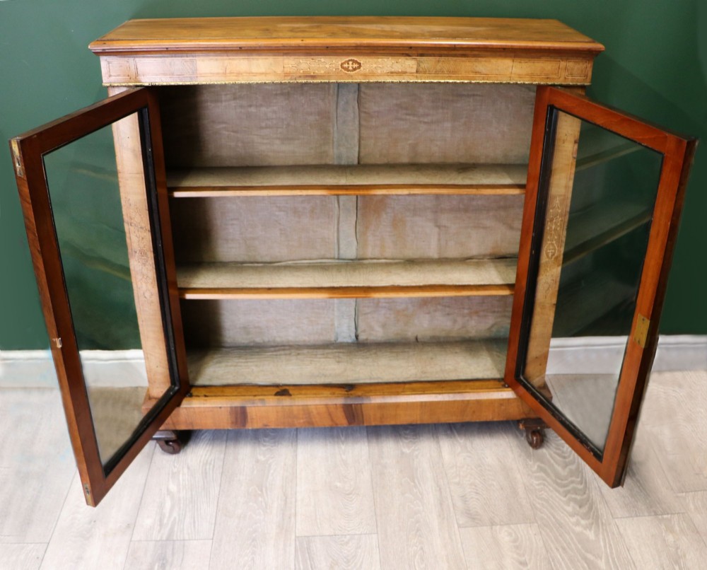 A mid-Victorian low walnut veneered bookcase featuring two glass glazed doors, marquetry inlay along the frieze, and brass trim detailing. View II