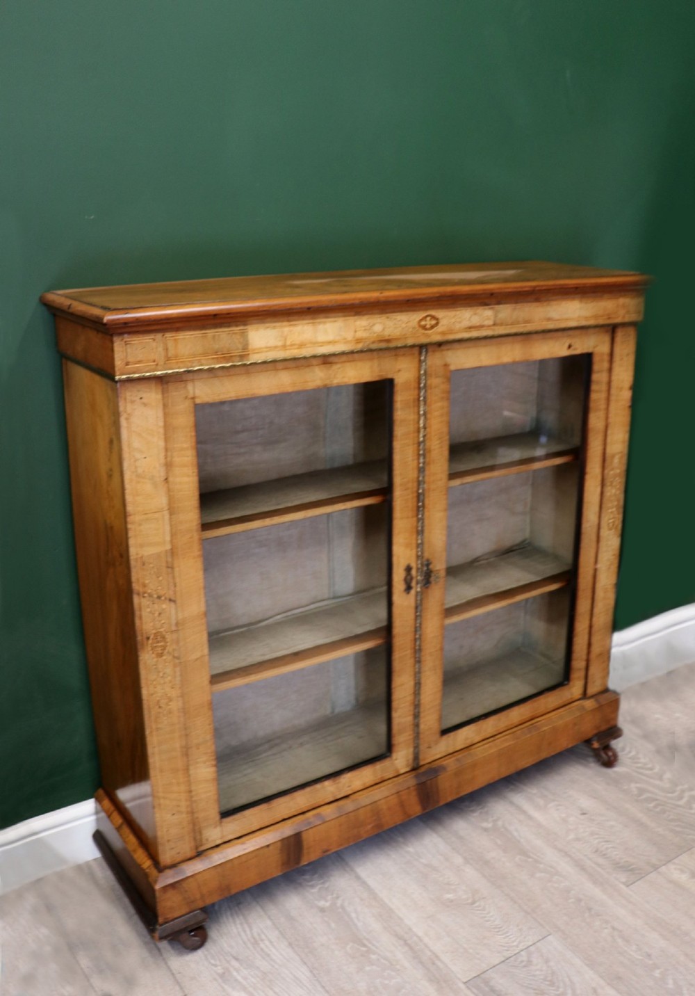 A mid-Victorian low walnut veneered bookcase featuring two glass glazed doors, marquetry inlay along the frieze, and brass trim detailing. View III
