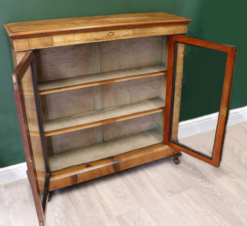 A mid-Victorian low walnut veneered bookcase featuring two glass glazed doors, marquetry inlay along the frieze, and brass trim detailing. View IV