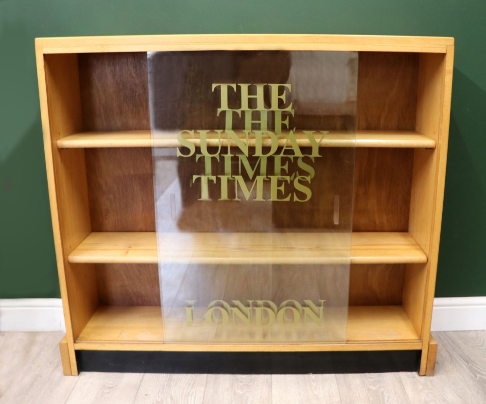 A low mid-century light oak bookcase with sliding glass doors featuring printed gold typography reading The Times and The Sunday Times London. View III