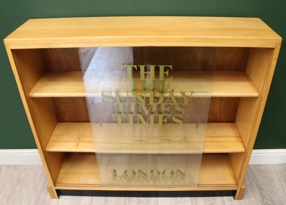 A low mid-century light oak bookcase with sliding glass doors featuring printed gold typography reading The Times and The Sunday Times London. View IV