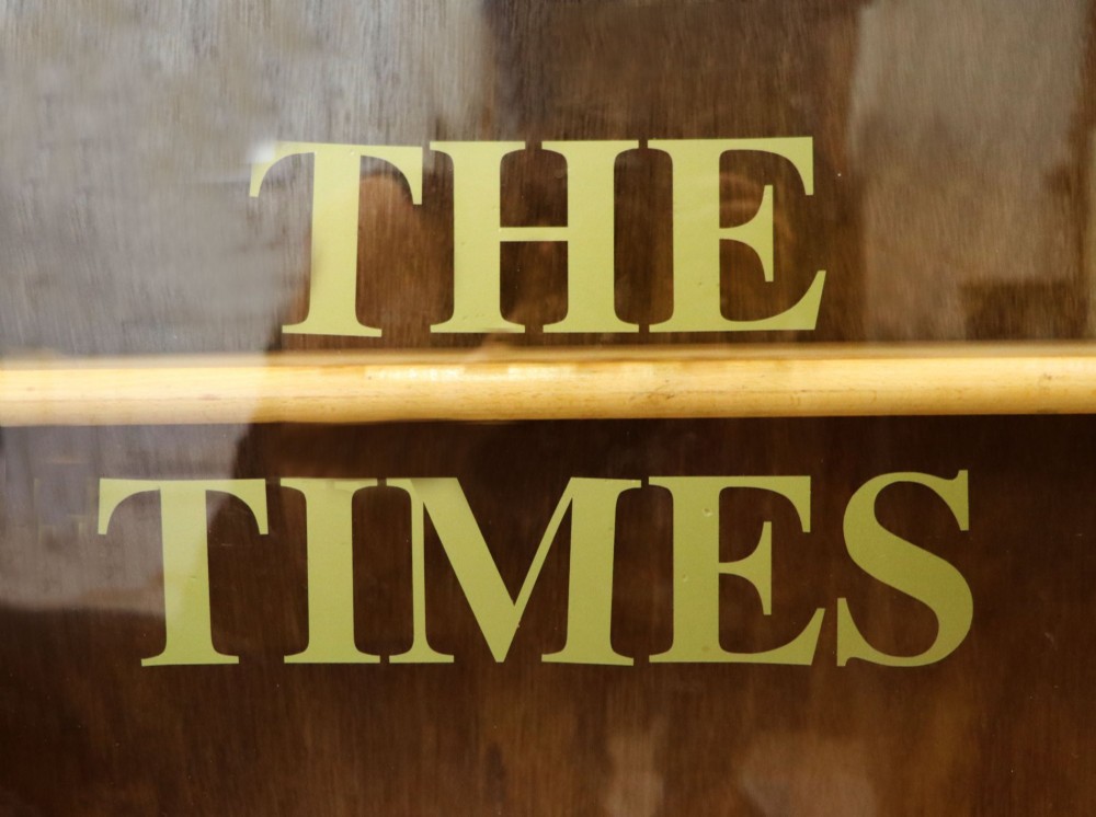A low mid-century light oak bookcase with sliding glass doors featuring printed gold typography reading The Times and The Sunday Times London. View VIII