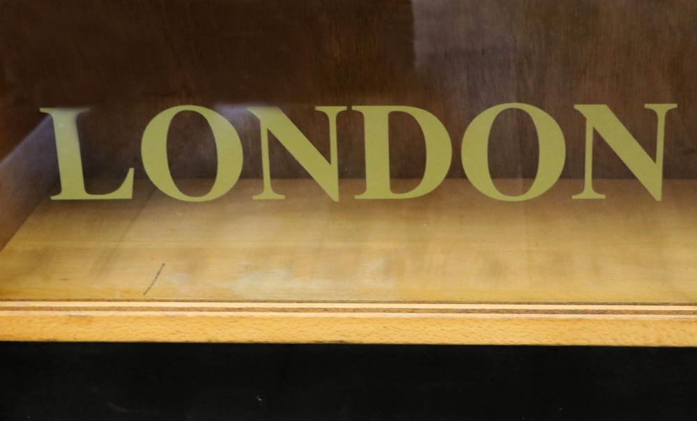 A low mid-century light oak bookcase with sliding glass doors featuring printed gold typography reading The Times and The Sunday Times London. View IX