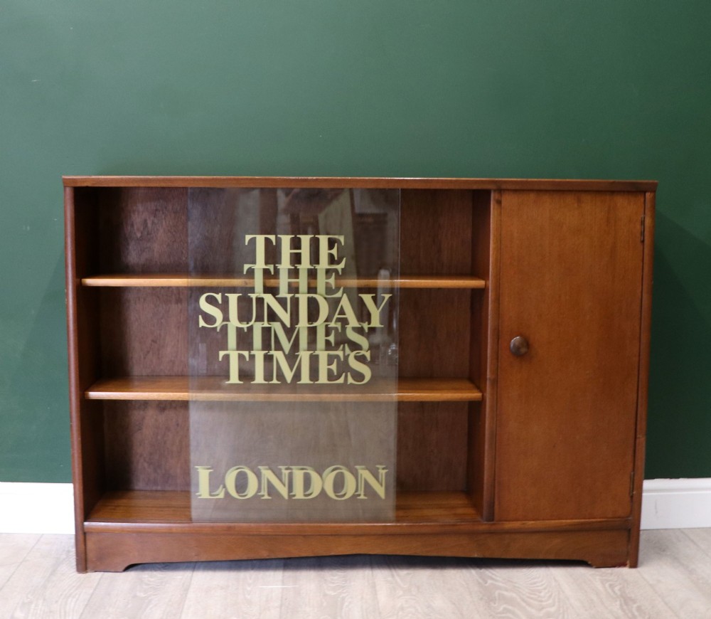 A low mid-century teak bookcase with two sliding glass doors featuring printed lettering alongside a single solid teak cupboard door. View III
